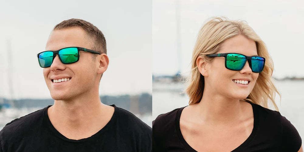 A close up image of a man's and woman's smiling faces looking in opposite directions wearing the Alpine Moon Blenders Sunglasses, showcasing a front view of the matte rubberized black and gloss green frame and polarized green mirrored lenses of the sunglasses.