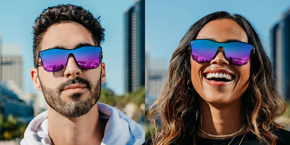 A close up image of a man's and woman's faces wearing the Black Forest Blenders Sunglasses, showcasing a front view of the gloss black and teal fade frame and polarized blue and purple mirrored PureBlend™ lenses of the sunglasses.