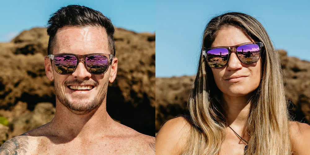 A close up front view image of a smiling man's and woman's faces wearing the Dream One Blenders Sunglasses, showcasing the glossy crystal gray frame and PureBlend™ lavender champagne mirrored lenses of the sunglasses.