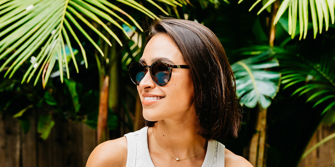 A close up, image of a woman in a white tanktop wearing the Tort Blenders Sunglasses, showcasing a front, left side view of the gloss tan tortoise frame and polarized PureBlend™ amber lenses of the sunglasses.